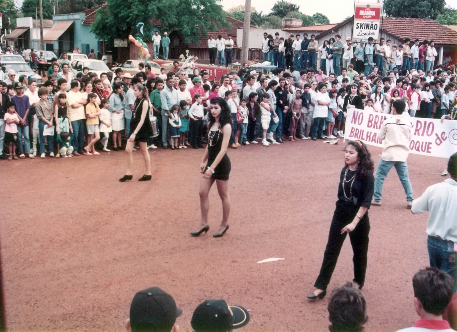 Desfile cívico na cidade de Rio Brilhante com pessoas caminhando em estrada de terra.
